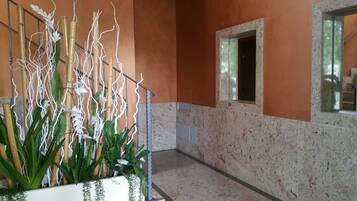 A hallway with a plant arrangement, a window, and a marble wall.