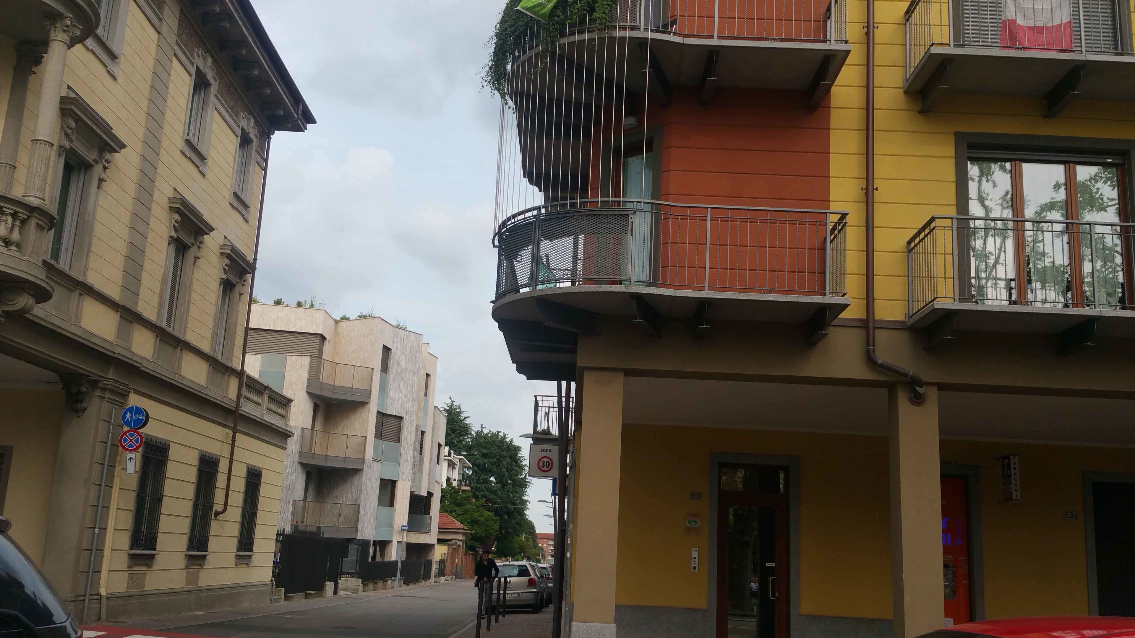 A multi-story building with a yellow facade, a balcony with metal railings, and a red door.