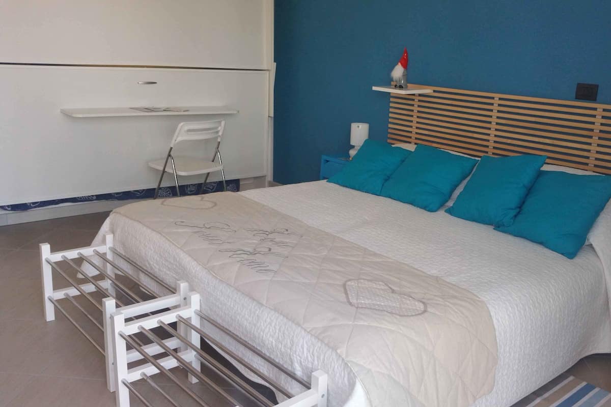 Un dormitorio con cama, mesita de noche, una silla y un estante con un objeto decorativo.