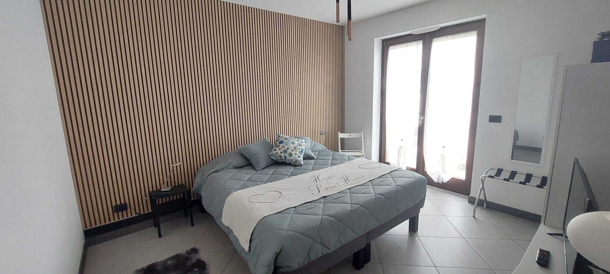 A modern bedroom with a bed, a bedside table, a chair, and a large window.