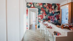 Una cocina moderna con papel tapiz floral, sillas blancas y una encimera larga.