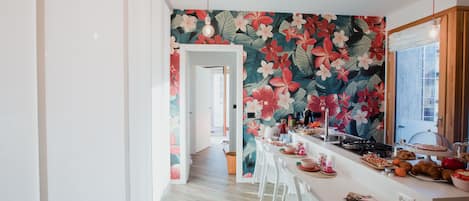 A modern kitchen with a floral wallpaper, white chairs, and a long counter.