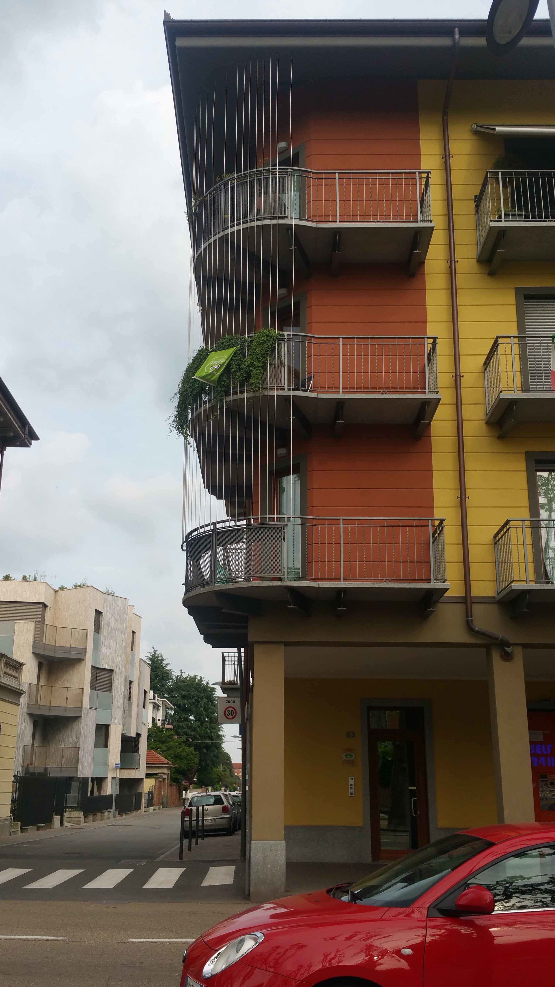 Un edificio de varios pisos con balcones, un paso de cebra y un coche rojo en primer plano.