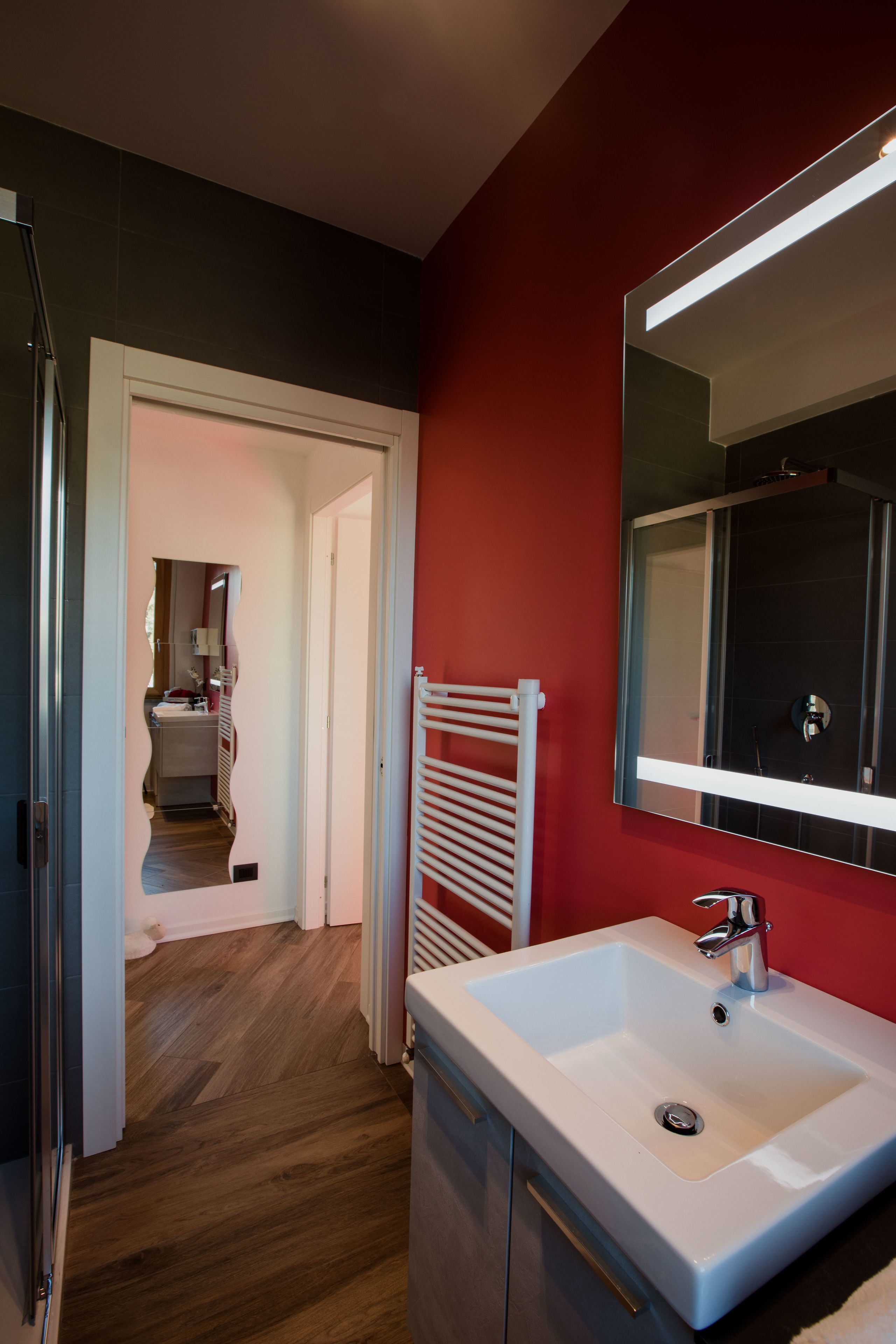 Ein Badezimmer mit einem weißen Waschbecken, einem Spiegel und einer roten Wand.