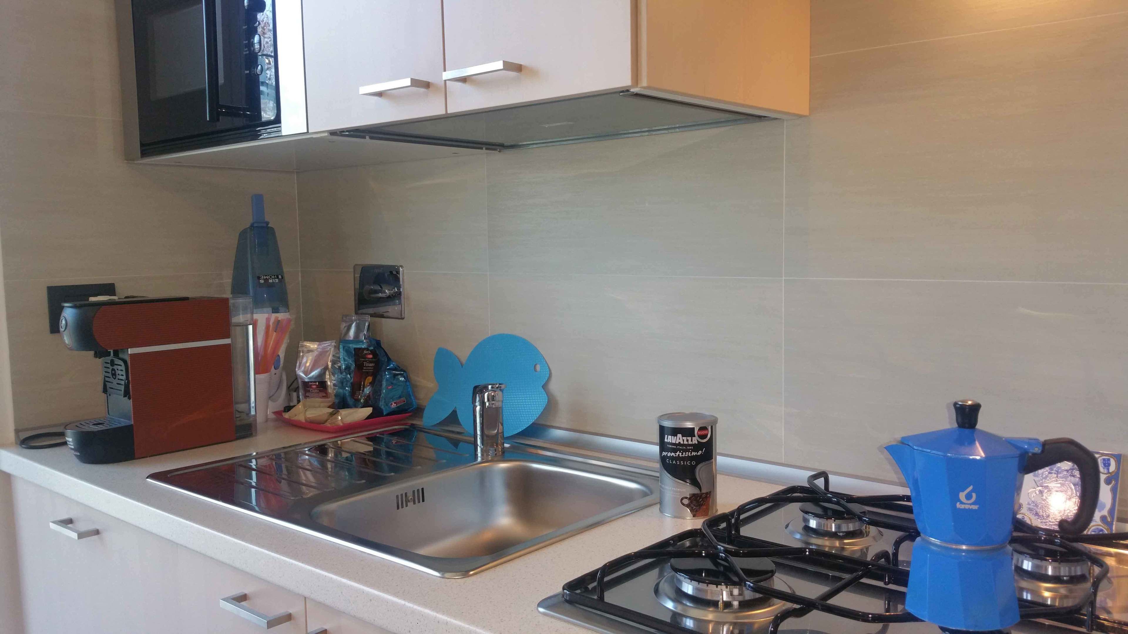 Una cucina moderna con un lavello in acciaio inossidabile, un piano cottura a gas con quattro fuochi e un forno a microonde sopra il piano cottura.