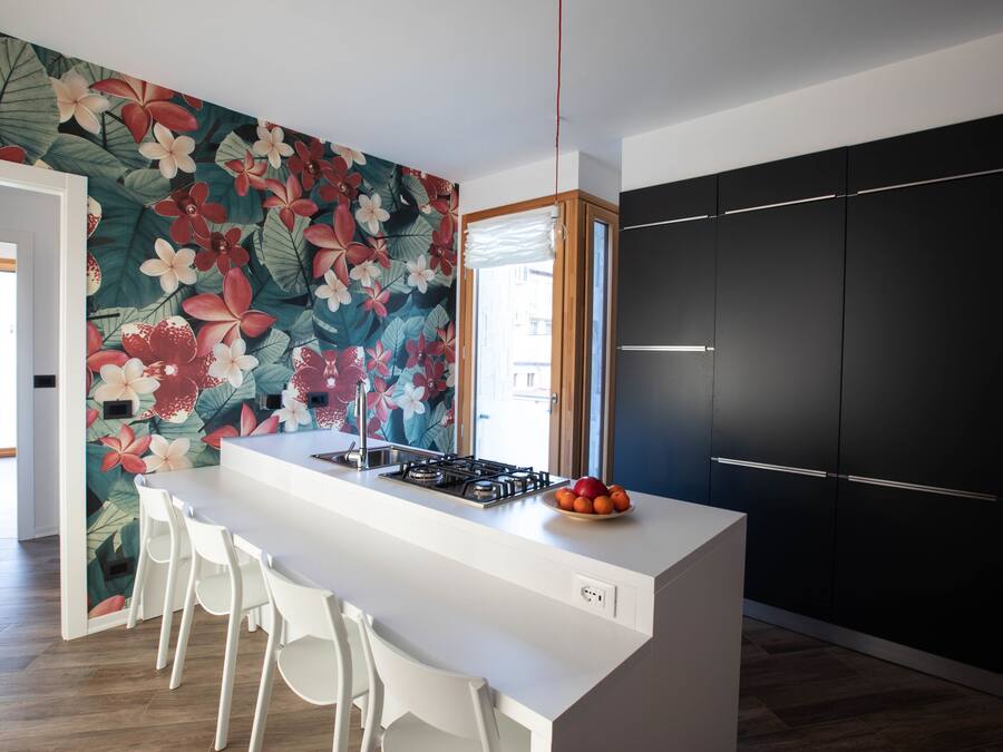 Una cucina moderna con isola centrale, sgabelli da bar bianchi, un armadietto nero e un murales floreale.