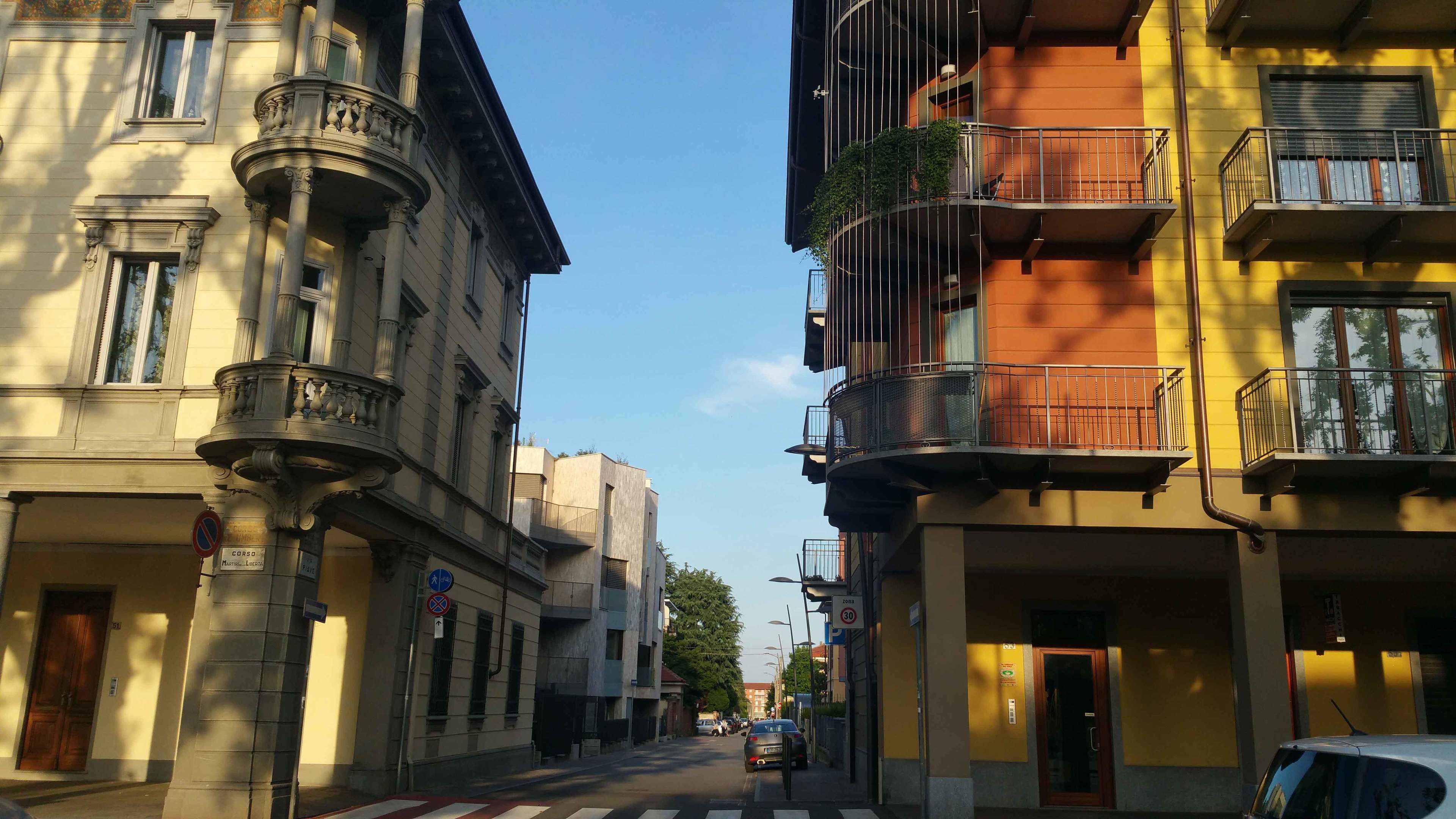 Vista de una calle con edificios que tienen balcones, cielo despejado y un paso de peatones.