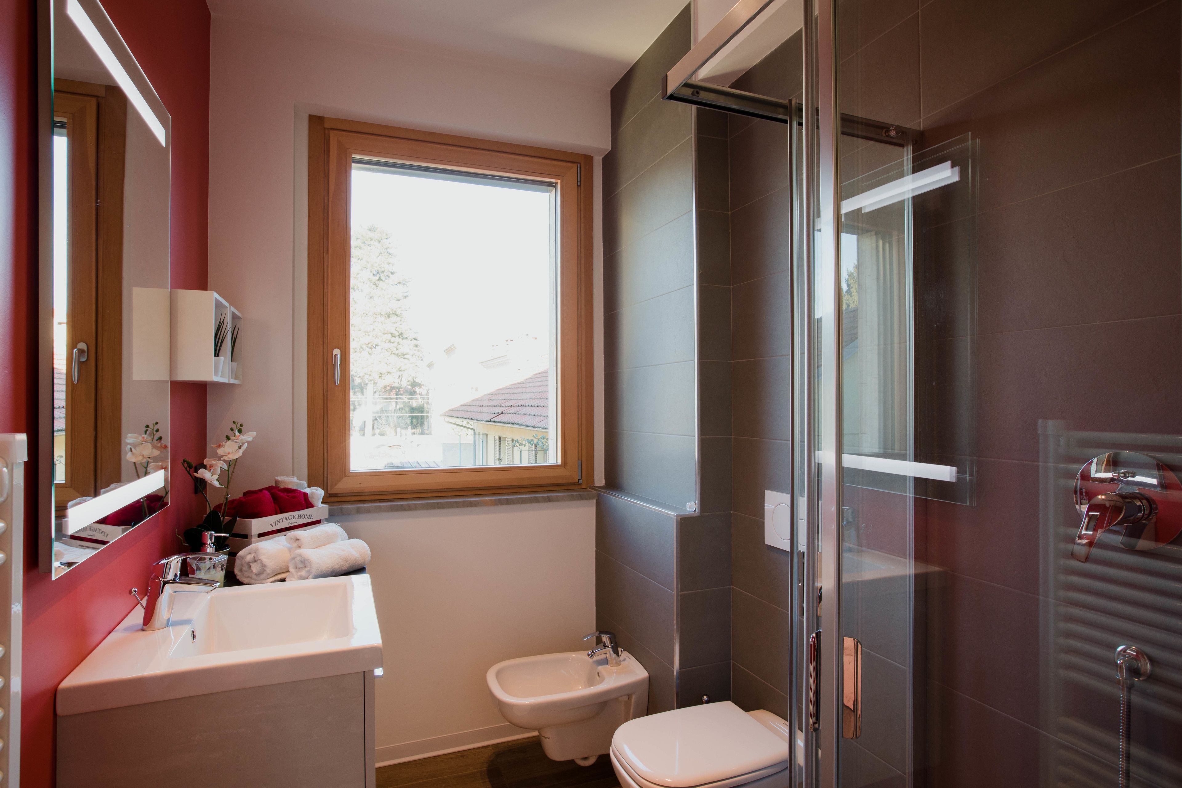 A modern bathroom with a large window, a bidet, a toilet, and a glass shower enclosure.