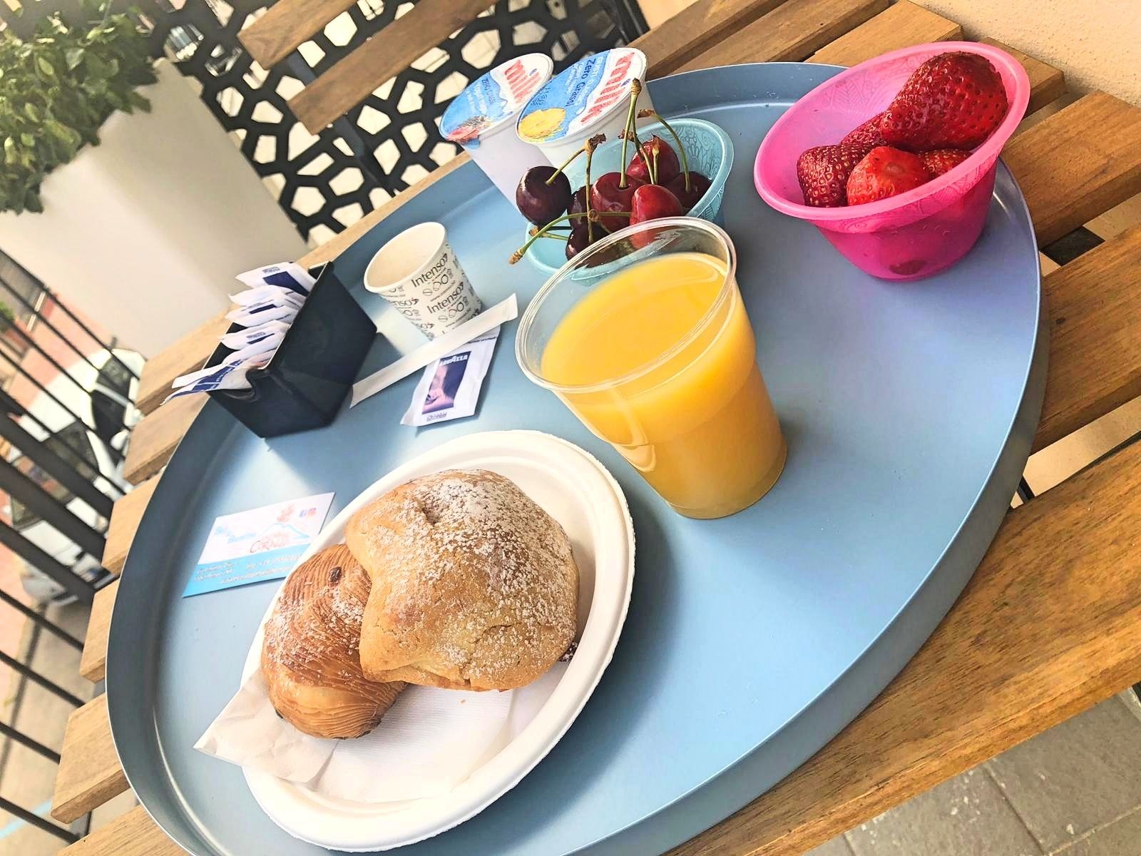 A tray with croissants, a glass of orange juice, a pink bowl with strawberries, a container of yogurt, and a packet of coffee creamer.