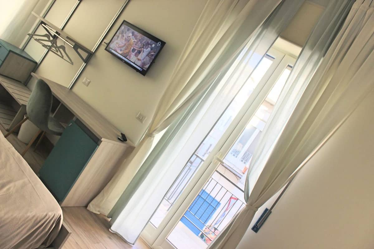 Ein Hotelzimmer mit Bett, Schreibtisch, Stuhl, Fernseher und einem Fenster mit Vorhängen.