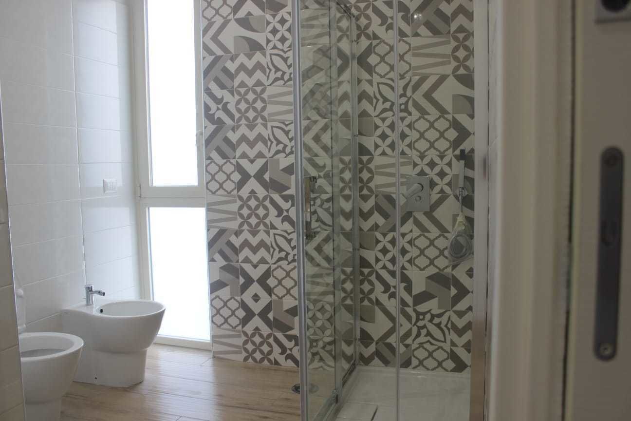 A bathroom with a bidet, a shower with a patterned glass door, and a large window.