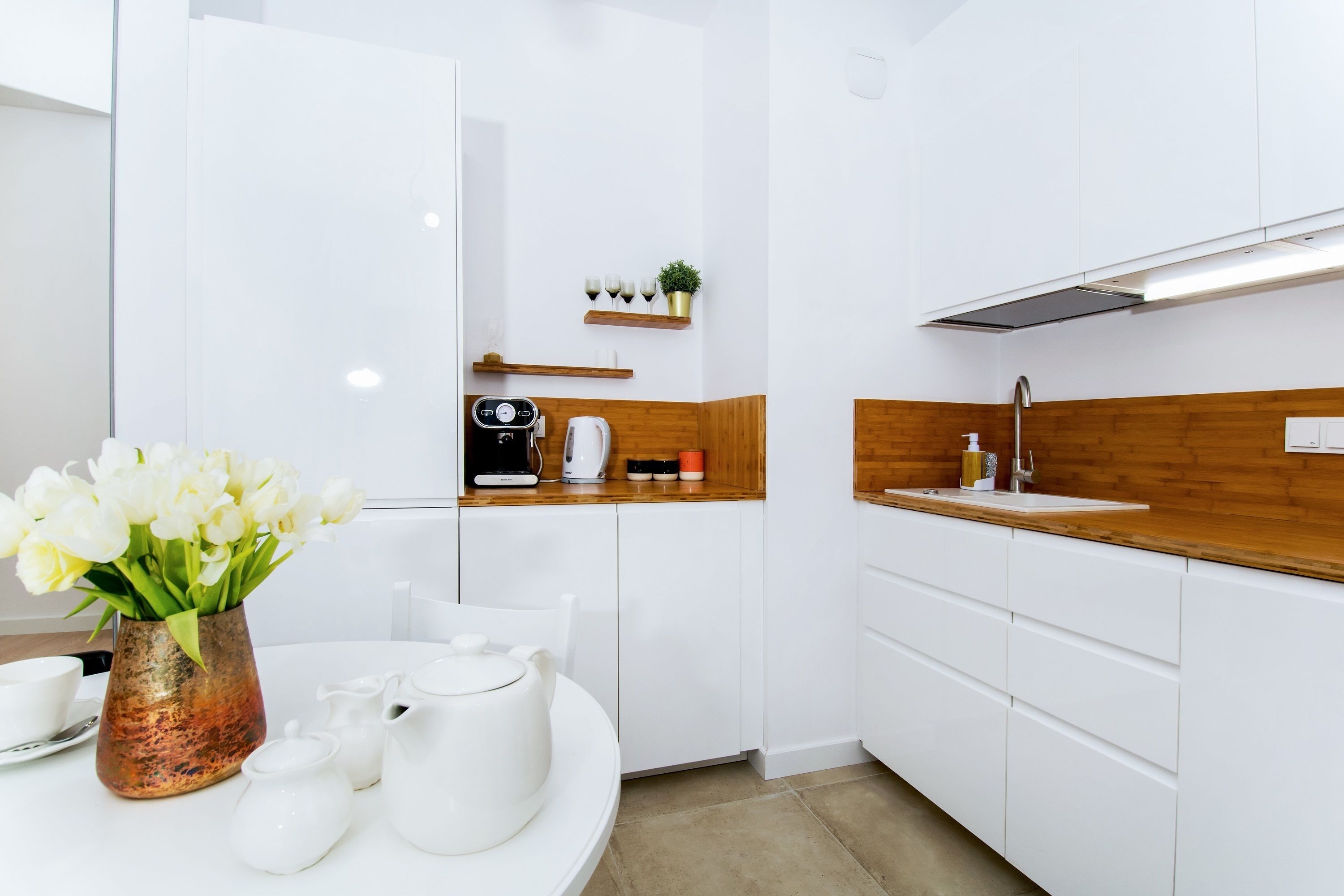 Une cuisine moderne avec des meubles blancs, un plan de travail en bois et une machine à café.