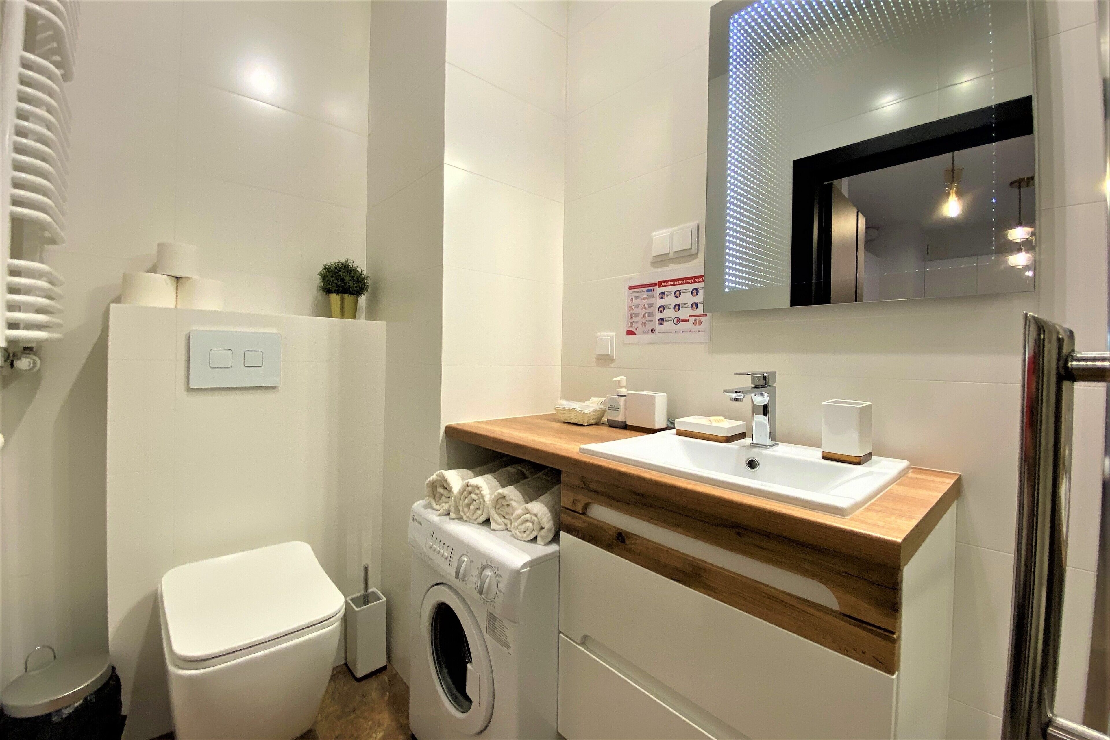Ein modernes Badezimmer mit Waschmaschine, Toilette, Waschbecken und Spiegel.
