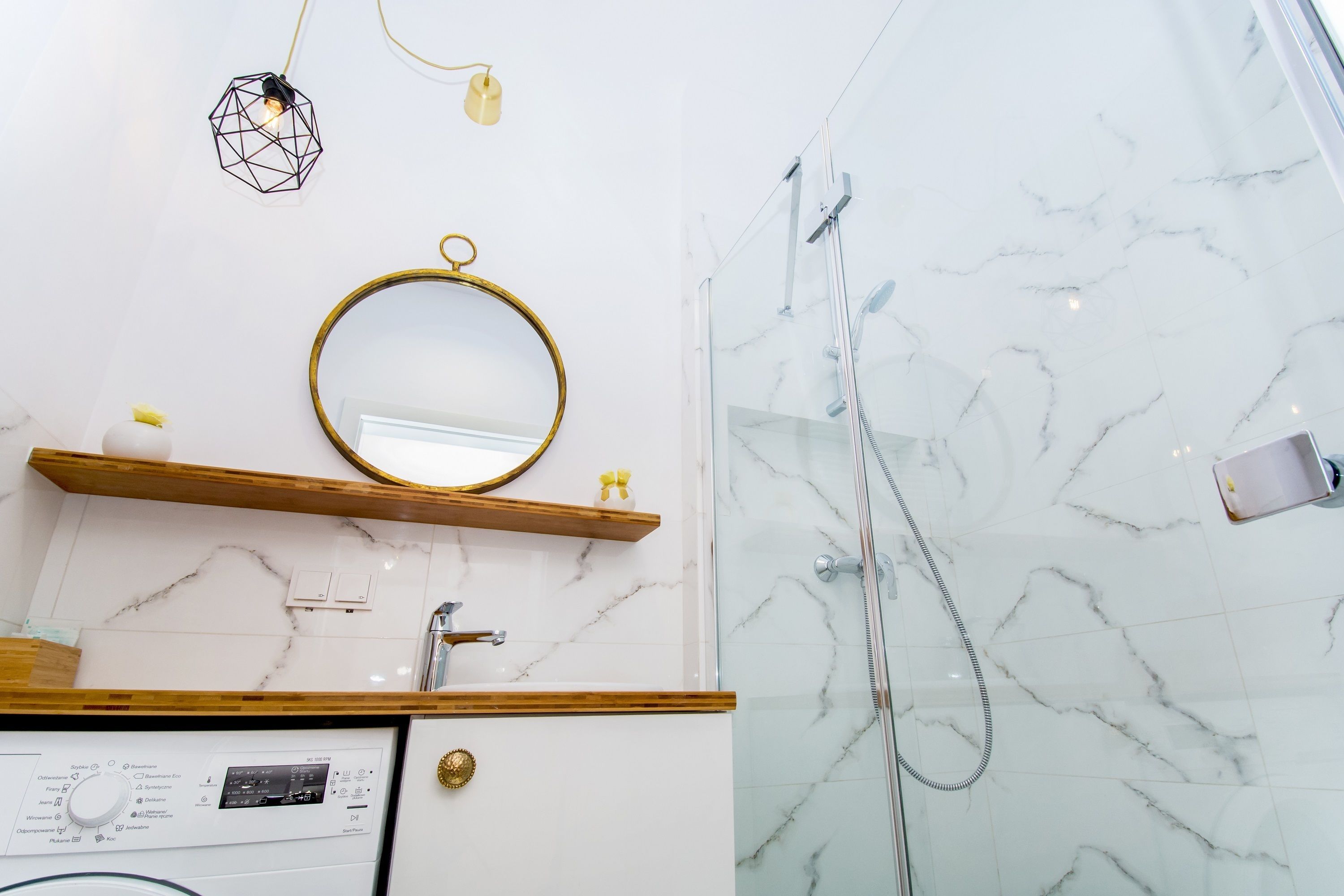 Une salle de bain avec un sol en marbre, un miroir rond, des étagères en bois, une douchette à main et un panneau de commande.