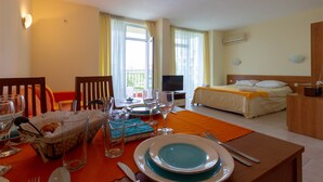 A hotel room with a dining area set for two, a bed, a TV, and a balcony with curtains. - Large Studio in Polo Resort (Sunny Beach)