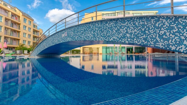 Une piscine avec un pont carrelé, une eau d’un bleu limpide et le reflet des bâtiments.