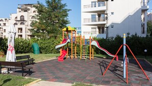 Une aire de jeux avec des toboggans et des structures d’escalade, des bancs et une zone dallée.