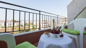 Un balcon avec une table dressée pour deux personnes, agrémentée d’un panier de fruits et d’une bouteille.