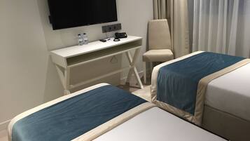 A hotel room with two beds, a desk with a flat-screen TV, a chair, and a curtain.