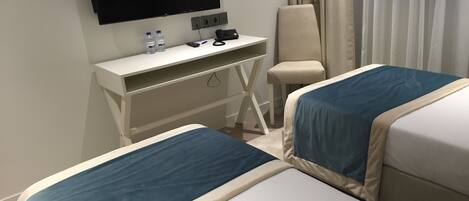 Une chambre d’hôtel avec deux lits, un bureau doté d’un téléviseur à écran plat, une chaise et un rideau.
