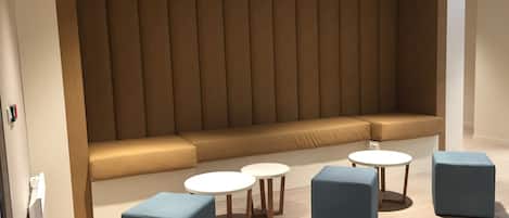 A modern seating area with a cushioned bench and three small round tables.