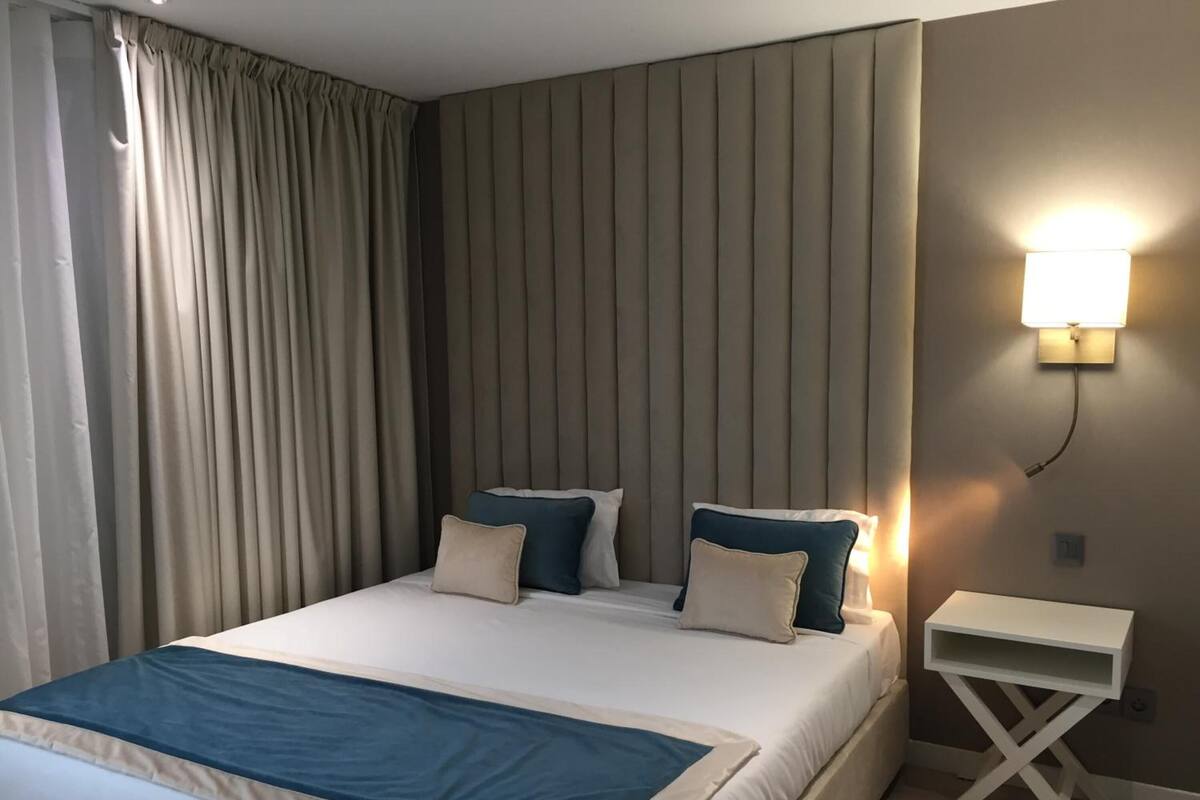 Een netjes opgemaakt bed met een blauw-witte dekbedovertrek, een nachtkastje en een wandlamp.