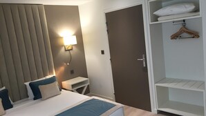A hotel room with a bed, bedside table, lamp, wardrobe, and a door.
