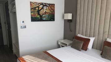 Una habitación de hotel con una cama, una mesita de noche, una lámpara y un cuadro de un árbol.