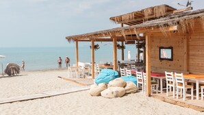 Una estructura de madera frente al mar con techo de paja, asientos al aire libre y vista al océano.