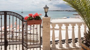 Una entrada con portón cerrado, un portón decorativo, un farol y vista a una playa con sombrillas y un barco a lo lejos.