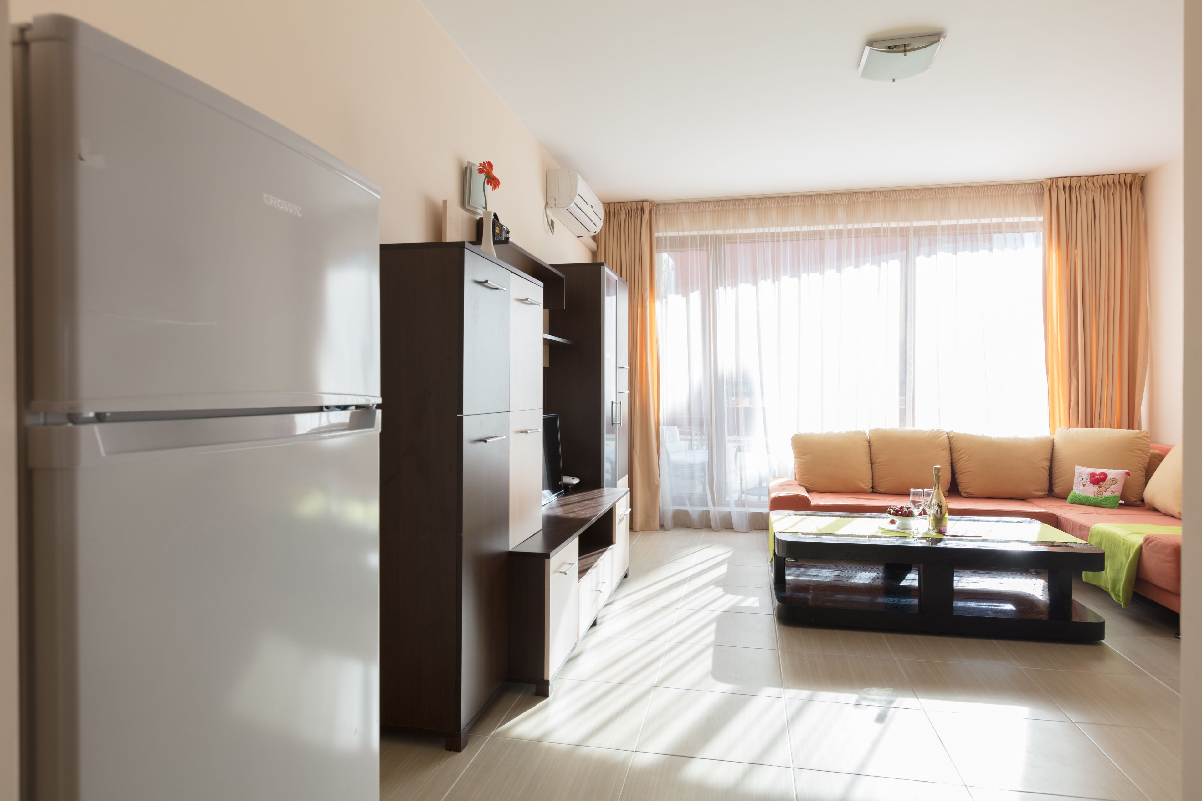 A modern living room with a sofa, a coffee table, and a kitchen area with a refrigerator and cabinets.