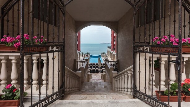 Una escalera conduce a una piscina con vista al mar, bordeada por barandales ornamentales y macetas con flores.
