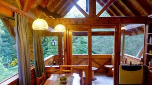 Une cabane en bois comprenant un coin repas, une cuisine et de grandes fenêtres donnant sur la forêt.