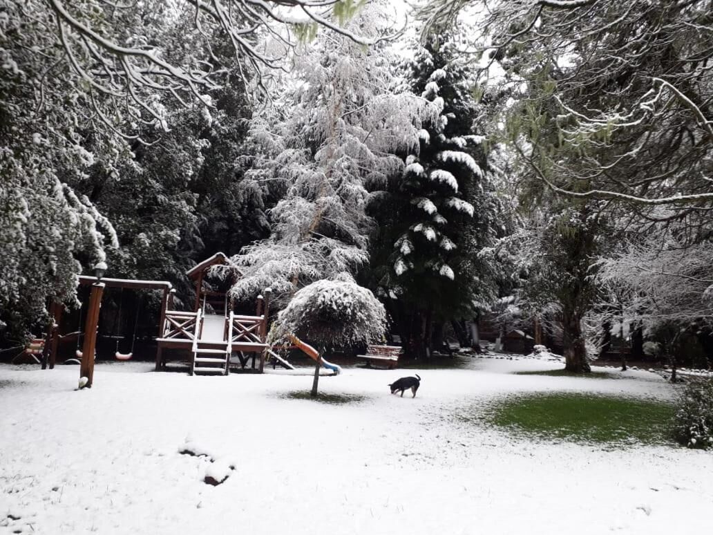 A snow-covered park with a swing set and a dog walking.
