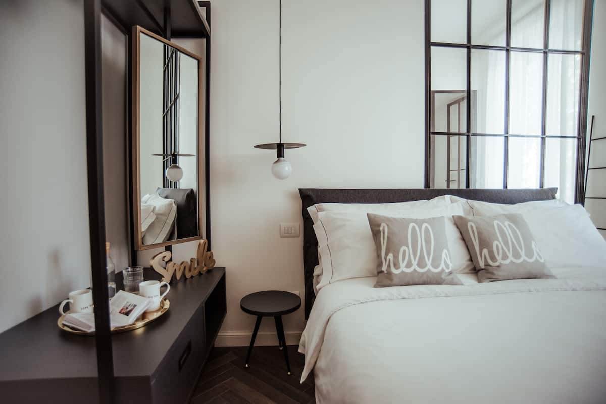A modern bedroom with a large bed, a bedside table with a tray of items, a mirror, and a window with a view.