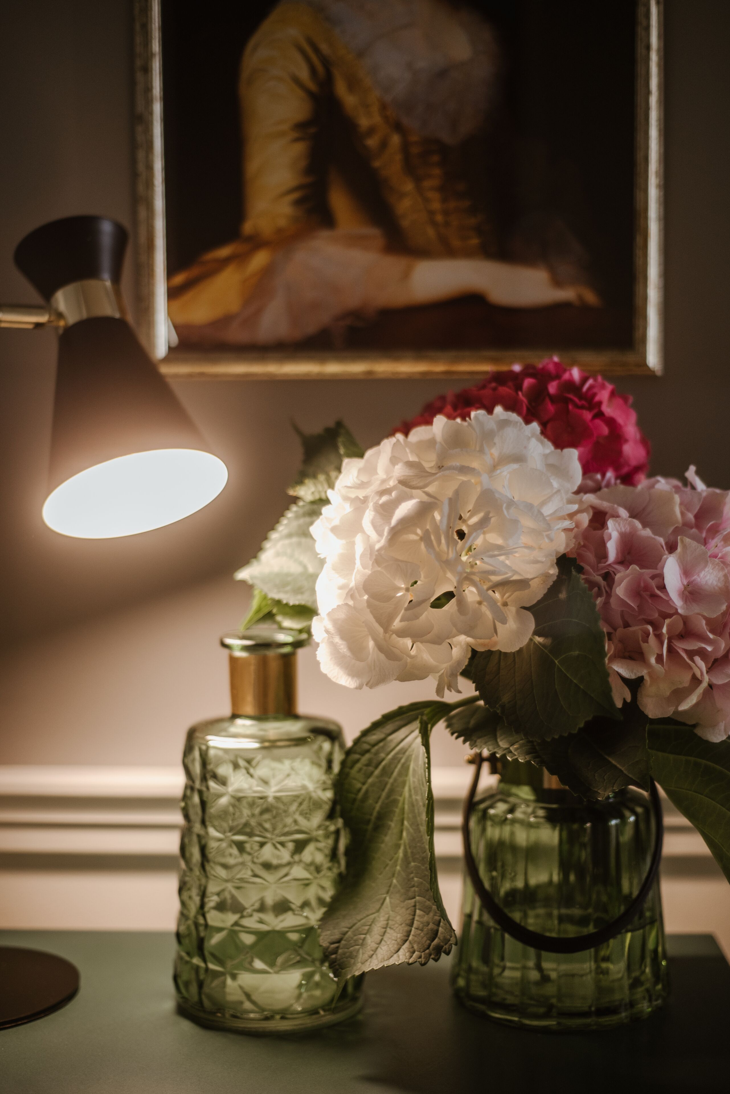 A table with a lamp, a glass vase with flowers, and a decorative bottle.