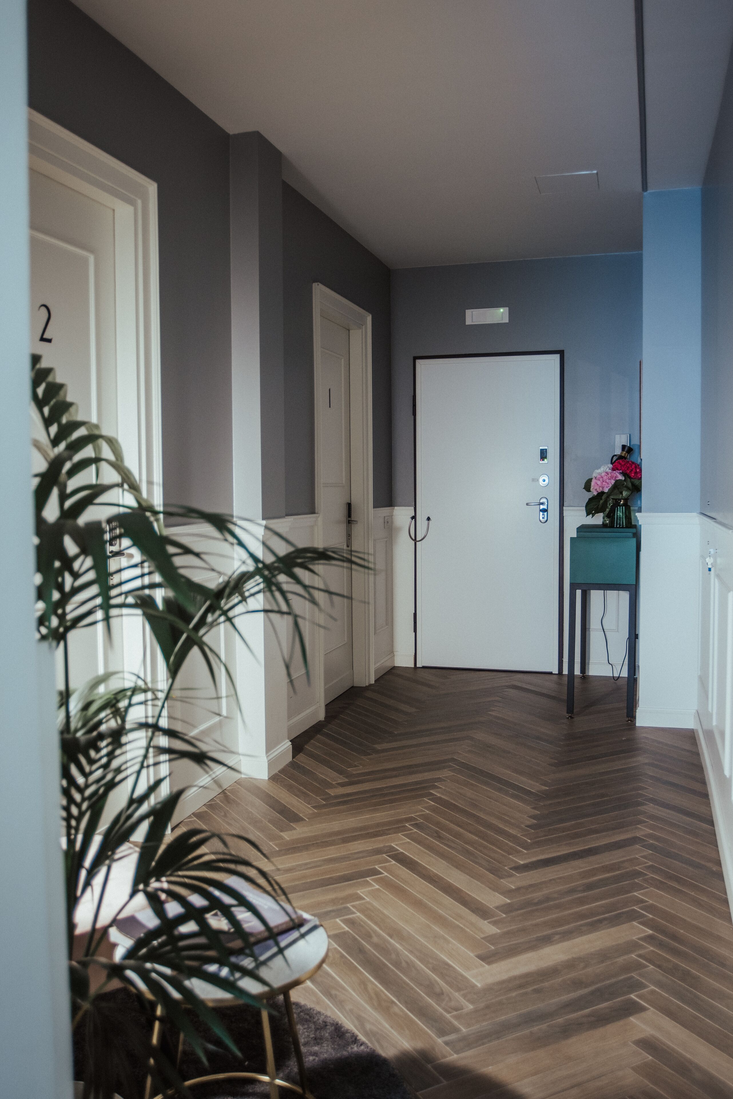 Um corredor com piso em padrão herringbone, portas brancas e uma pequena mesa com um vaso de flores.