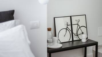 A modern bedroom with a bed, a bedside table with a framed bicycle artwork, a mirror, and a suitcase.