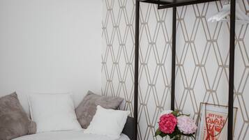 Une chambre à coucher comprenant un lit, une table de chevet, une lampe fixée au mur et un papier peint à motifs géométriques.