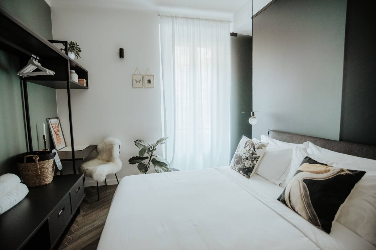 A modern bedroom with a large bed, a dresser, a chair, and a plant.