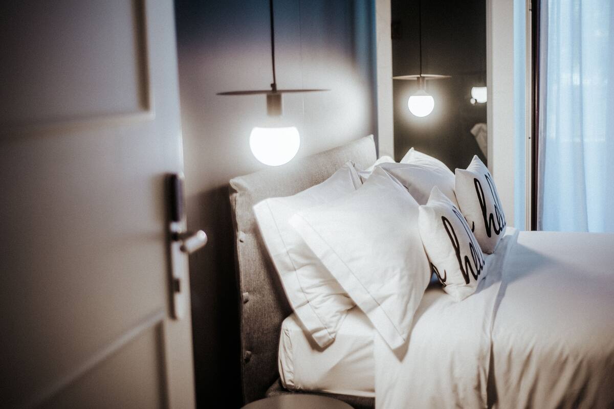 A hotel room with a neatly made bed, a nightstand, and a hanging light fixture.