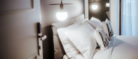 Una habitación de hotel con una cama bien hecha, una mesita de noche y una lámpara colgante.