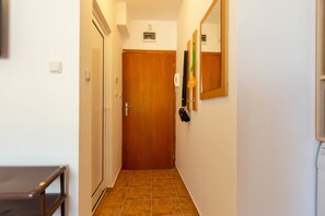 A narrow hallway with a wooden door at the end, a small table on the left, and a mirror on the right wall. - Apartment in Vista Del Mar (Ravda)