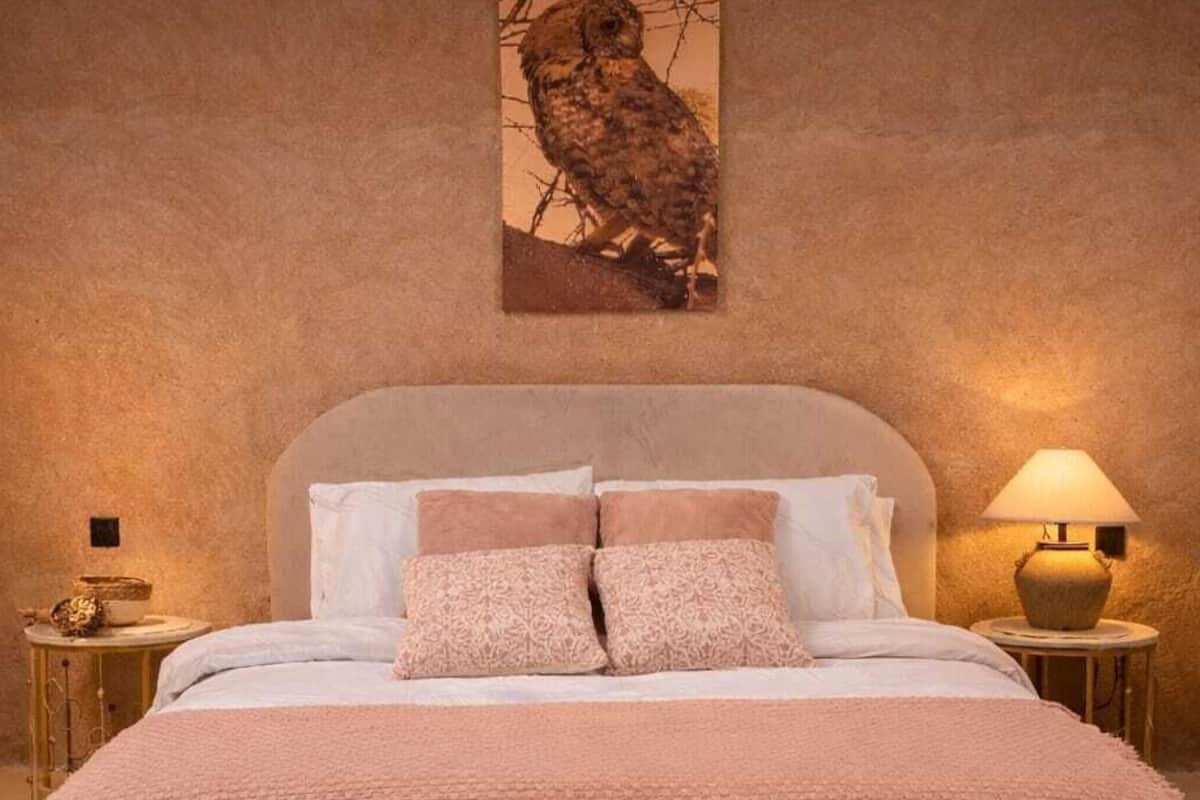 A bedroom with a bed, pillows, a wall-mounted owl artwork, bedside tables with lamps, and a textured ceiling.