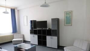Un salon moderne avec un canapé, une table basse en verre, un téléviseur posé sur un meuble et un radiateur.