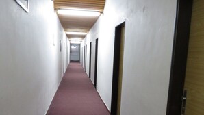 Un long couloir étroit aux murs blancs, au plafond orné de panneaux de bois et recouvert d’un tapis rouge.