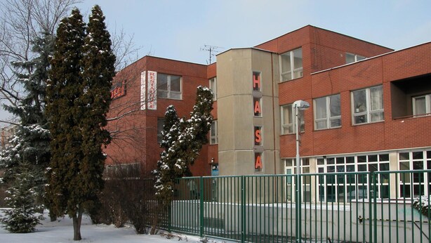 Un bâtiment à la façade en briques rouges, une clôture en métal vert et un sol recouvert de neige.