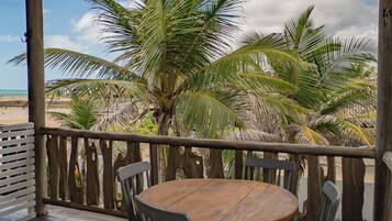 A wooden deck with a table and chairs, overlooking a beach with palm trees.