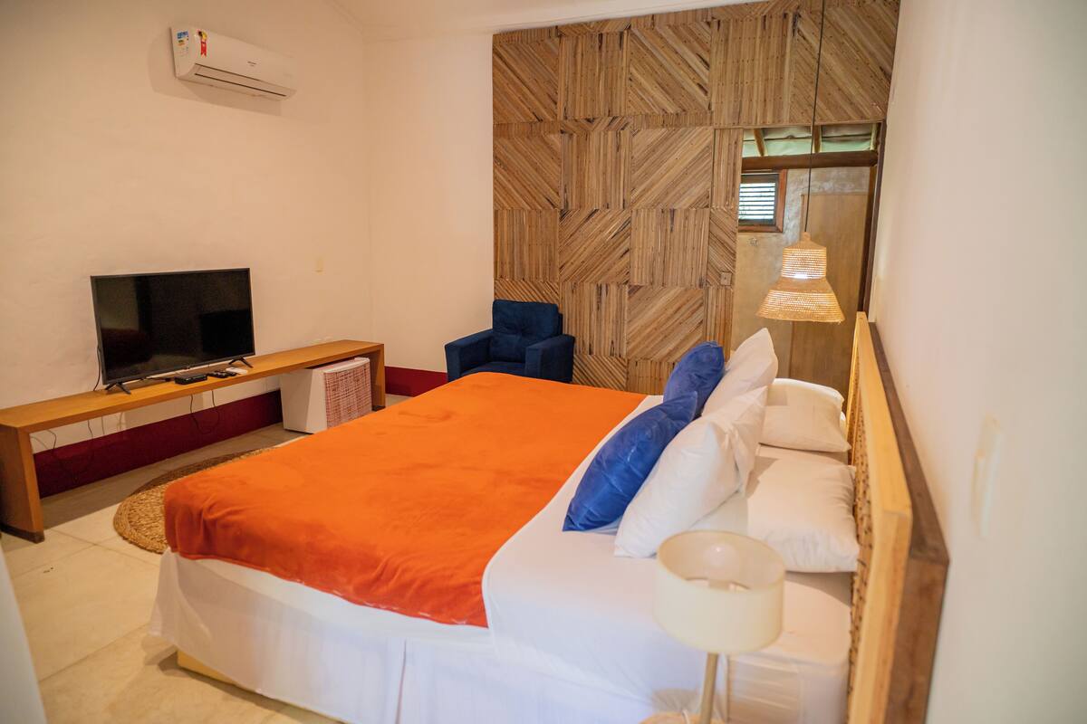 Ein Schlafzimmer mit einem Bett, einem Fernseher, einem Sessel, einer Lampe und einer Wandklimaanlage.