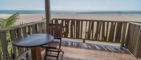 A wooden deck with a table and chairs overlooking a beach.